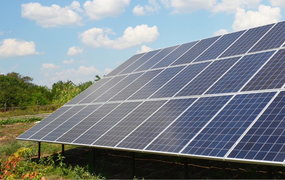 A large ground-mounted solar array in a field under a blue sky