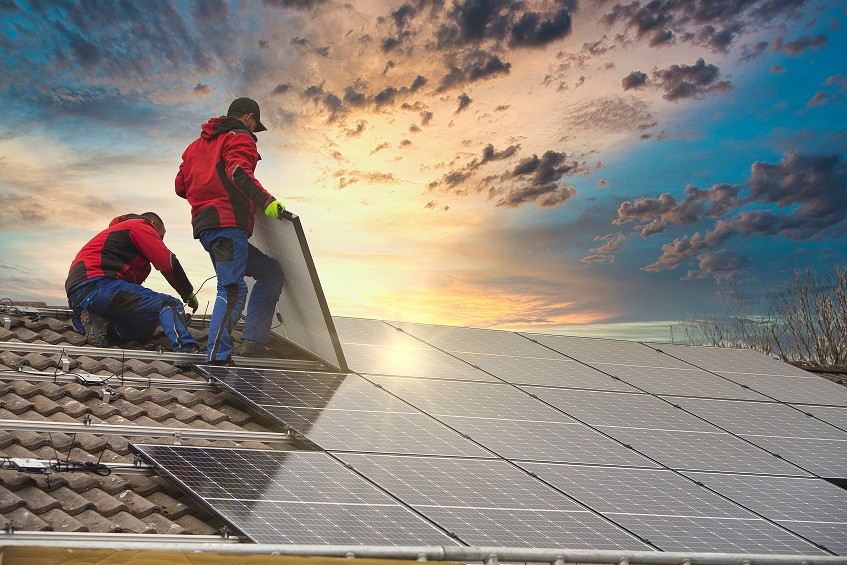 Two installers fitting solar panels on a tiled roof at sunset